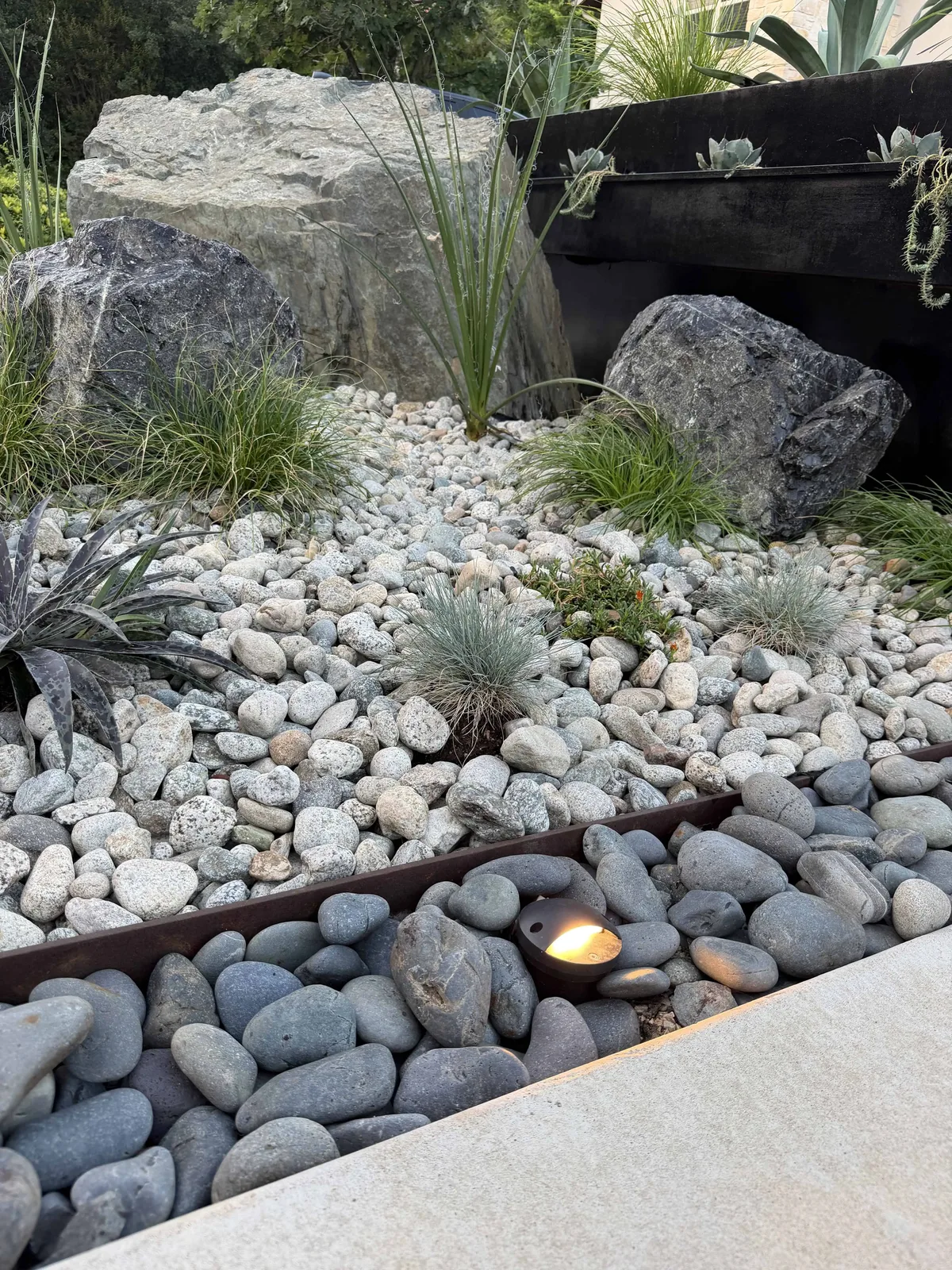 Planting bed detail with boulders, native sedge, Mexican beach pebbles, and low-voltage lighting — Tarrytown Austin TX